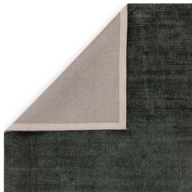 Dark textured area rug with beige edging and corner folded to show backing