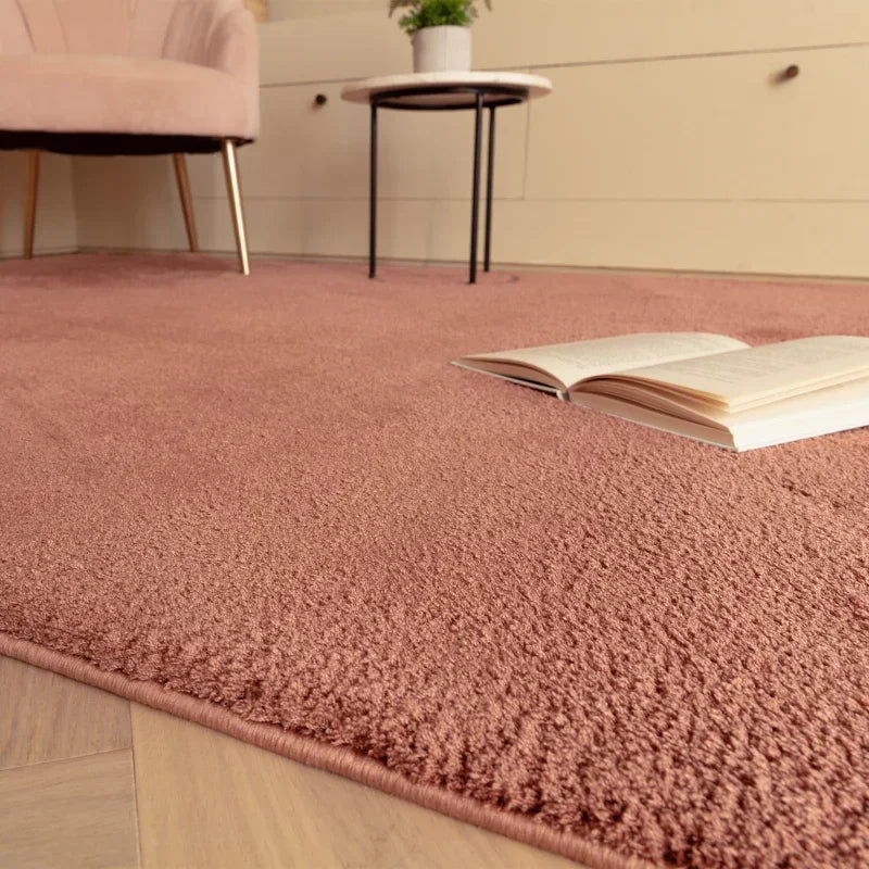 Blush pink area rug in living room with open book, accent chair and side table