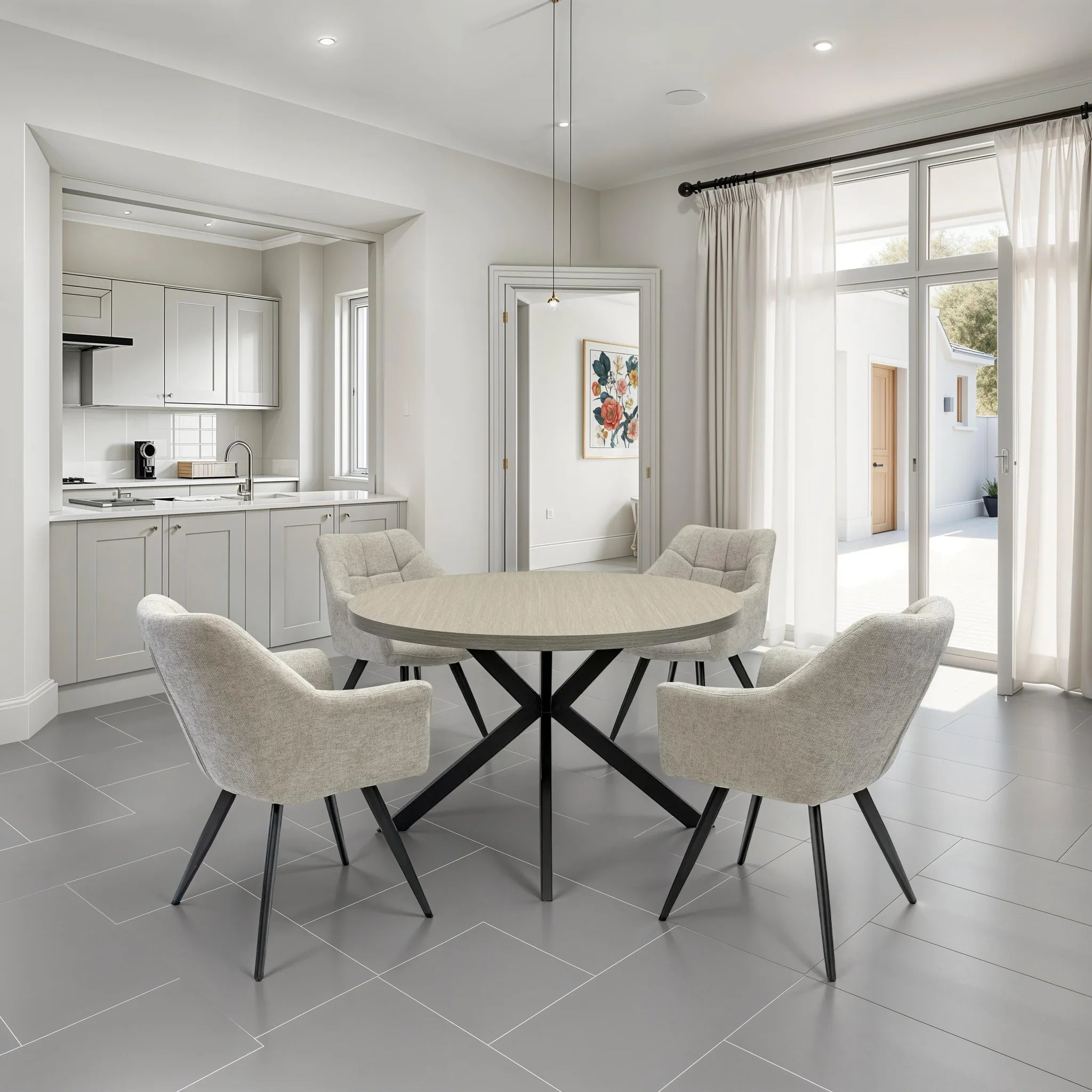 A modern dining room setup featuring a round light beige stone dining table with a black X-shaped base, surrounded by four upholstered dining chairs in a light beige textured fabric with black legs. The room has light gray tiled floors, white walls, and large windows with sheer curtains.