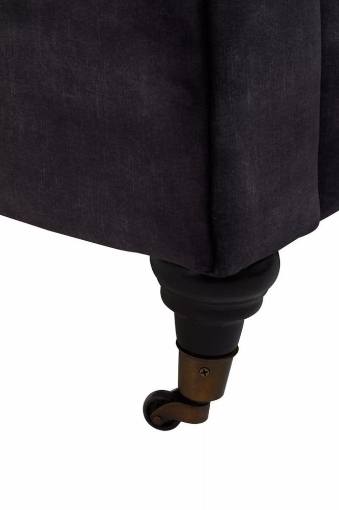 Close-up view of the leg of a grey velvet sofa, showcasing a dark wooden foot with a rounded design. The fabric appears soft and plush, highlighting the texture of the velvet material
