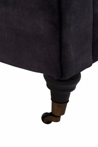 Close-up view of the leg of a grey velvet sofa, showcasing a dark wooden foot with a rounded design. The fabric appears soft and plush, highlighting the texture of the velvet material