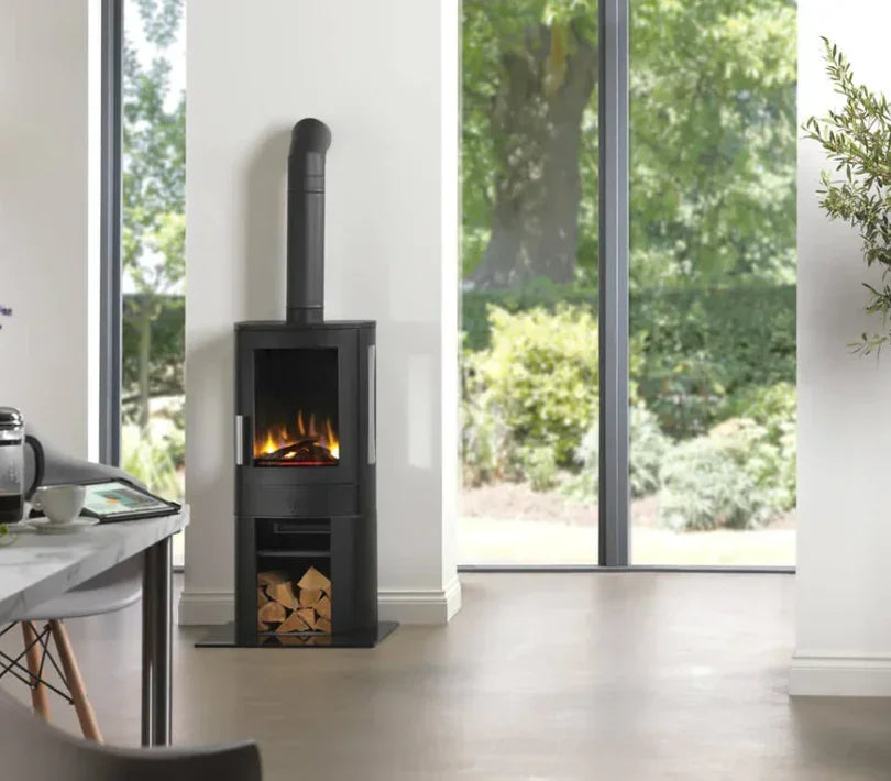 Black wood burning stove with fire and log storage beside large window in living room