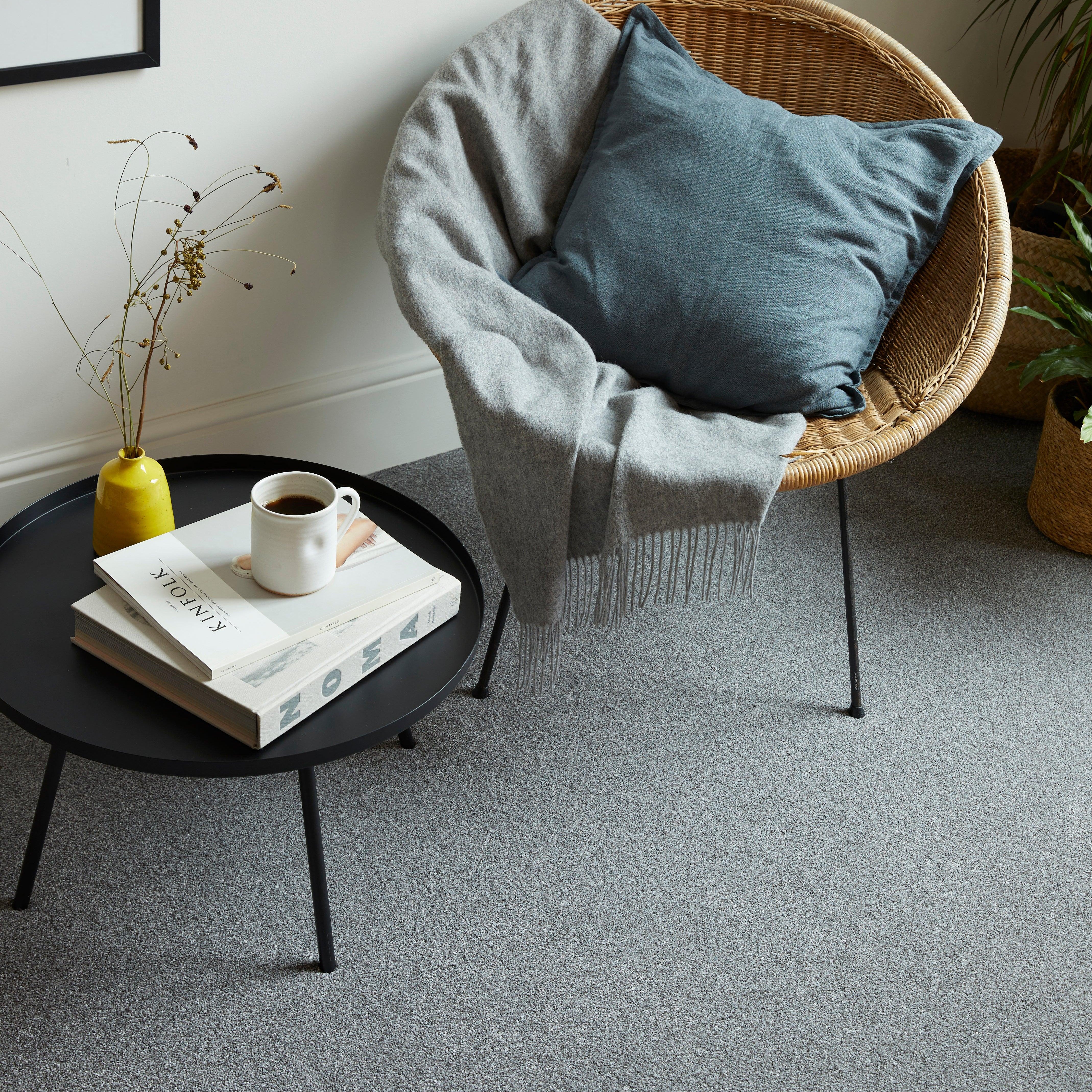 Grey carpet in a living room with a round black table and wicker chair
