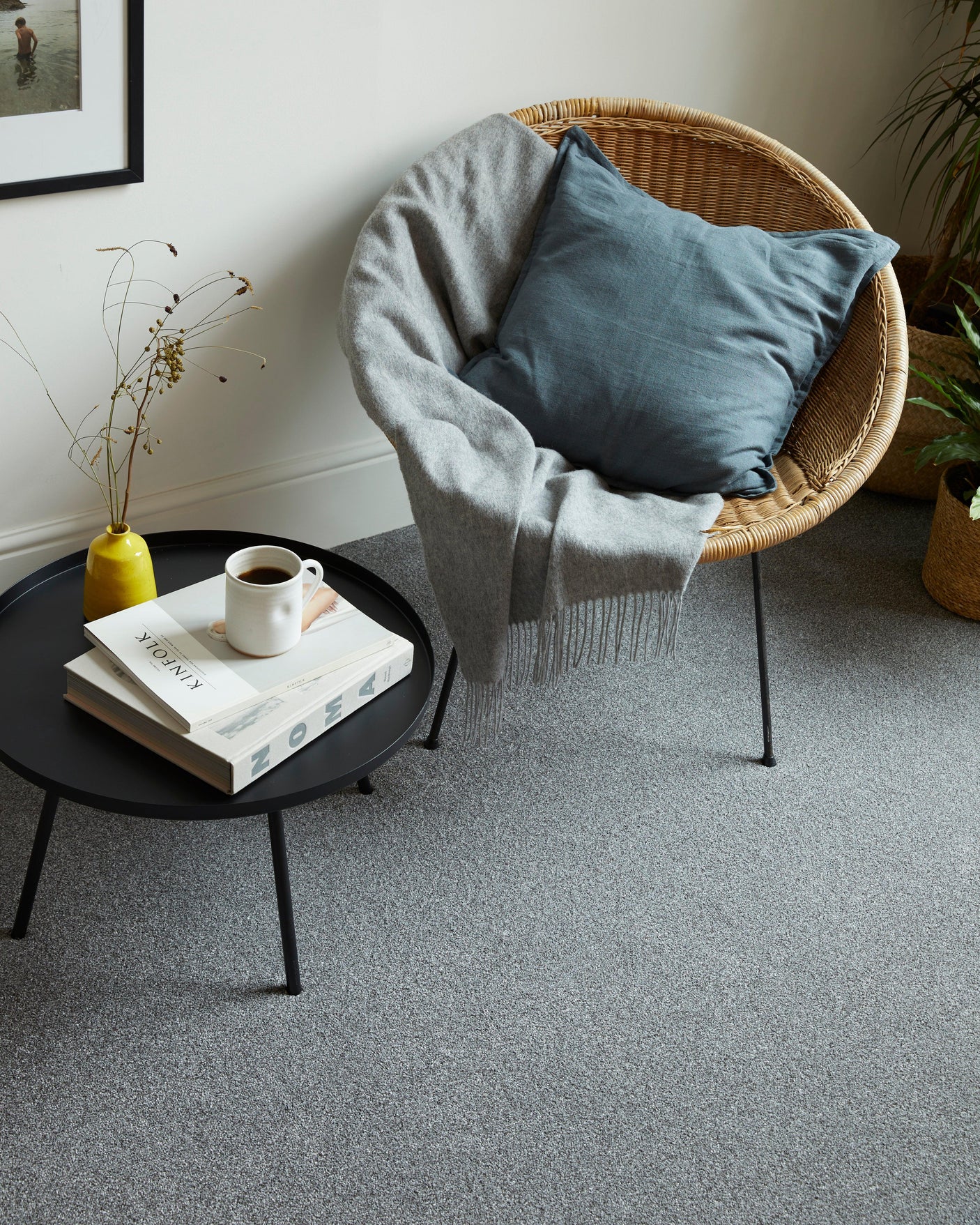 Grey carpet in a living room with a round black table and wicker chair