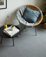 Grey carpet in a living room with a round black table and wicker chair