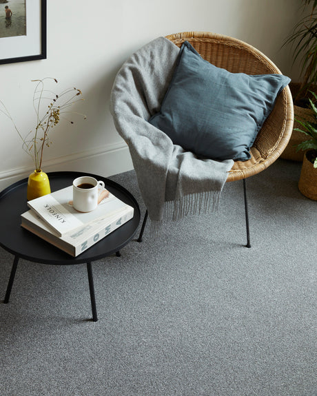 Grey carpet in a living room with a round black table and wicker chair