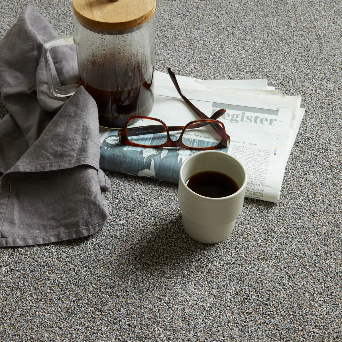 Grey speckled carpet styled with coffee cup, glasses, and newspaper — casual setting