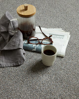 Grey speckled carpet styled with coffee cup, glasses, and newspaper — casual setting