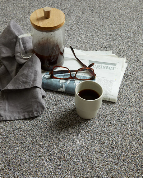 Grey speckled carpet styled with coffee cup, glasses, and newspaper — casual setting