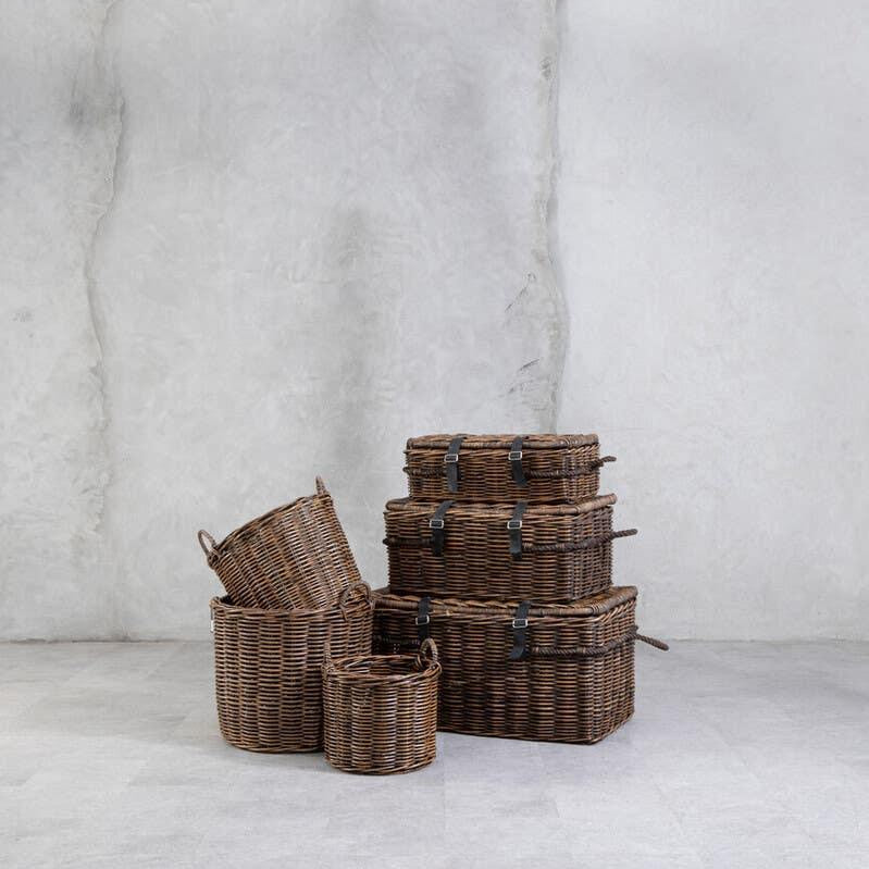 Stacked brown wicker storage baskets with lids and handles on grey floor