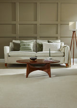 Light grey sofa with patterned cushions in a paneled living room, paired with a wooden coffee table.