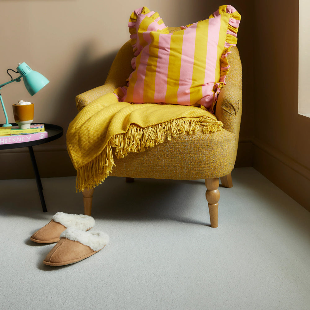Yellow upholstered armchair with pink striped cushion and fringed throw in cozy room setting