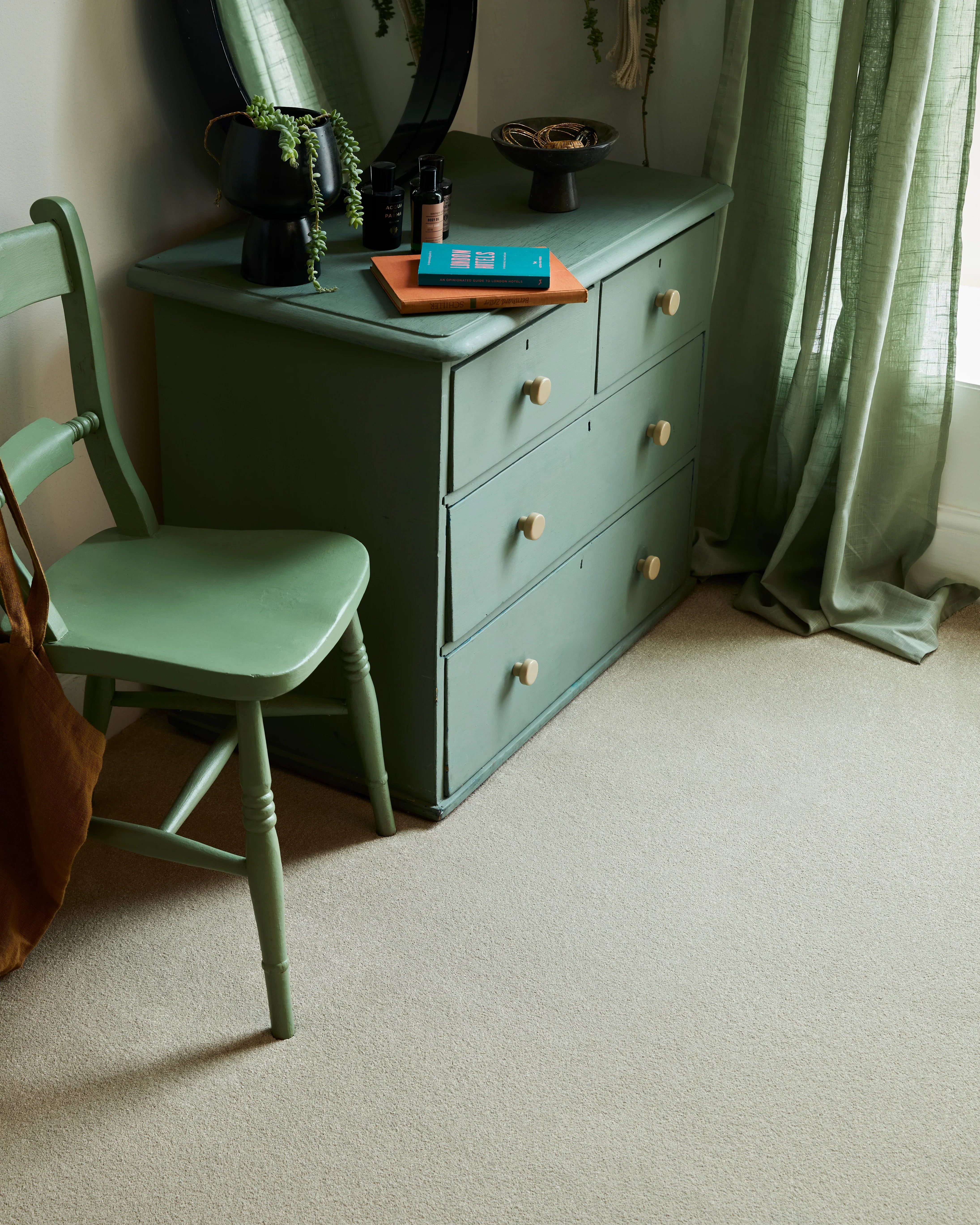 Sage green wooden dresser and chair in a softly lit room with sheer green curtains